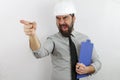 Bearded architect wearing safety helmet and holding clipboard in hand pointing with finger screaming and shouting Royalty Free Stock Photo