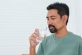 Bearded Asian man wearing comfortable pajamas on holiday morning The man picked up a glass of clean water that had been poured Royalty Free Stock Photo