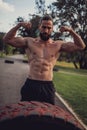 Bearded athlete showing biceps in front of the workout tire