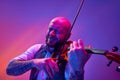 Bearded bald man, musician emotionally playing violin against gradient purple background in neon light. Solo performance Royalty Free Stock Photo