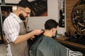 Bearded barber cutting hair of male customer. Hairstylist serving client at barber shop. Royalty Free Stock Photo