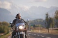 Bearded biker in black leather jacket on modern motorcycle on country roadside.