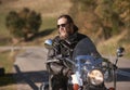 Bearded biker with long hair in black leather jacket and sunglasses sitting on modern motorcycle. Royalty Free Stock Photo