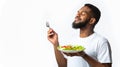 Bearded Black Guy Enjoying Vegetable Salad Standing Over White Background