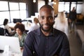 Bearded black male creative standing in a busy casual office, smiling to camera Royalty Free Stock Photo