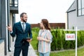 Bearded broker holding clipboard and gesturing near attractive woman and board with sale letters