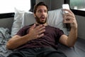 A bearded brown haired hypster man wearing a red t-shirt lays down relaxing on his bed in his camper talking to someone on his