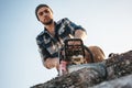 Bearded brutal lumberjack wearing plaid shirt sawing tree with chainsaw for work on sawmill Royalty Free Stock Photo