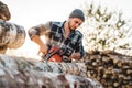 Bearded brutal lumberjack wearing plaid shirt sawing tree with chainsaw for work on sawmill Royalty Free Stock Photo