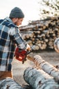 Bearded brutal lumberjack wearing plaid shirt sawing tree with chainsaw for work on sawmill. Wooden sawdust fly apart Royalty Free Stock Photo