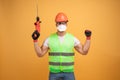 Bearded builder in helmet, reflective vest, glasses and gloves and protective mask, holds drill in his hands and looks happily