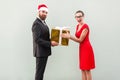 Bearded businessman in christmas hat give a present beautiful woman in red dress with amazed face.