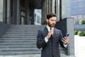 Bearded businessman in a formal suit, talking on video call using smartphone on urban city street confident business man, Royalty Free Stock Photo