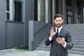 Bearded businessman in a formal suit, talking on video call using smartphone on urban city street confident business man, Royalty Free Stock Photo