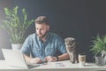 Bearded businessman sits in office at table and uses laptop, next sits gray cat.