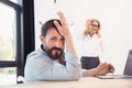 Bearded businessman using laptop while blonde businesswoman working with whiteboard behind Royalty Free Stock Photo