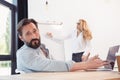 Bearded businessman using laptop while blonde businesswoman working with whiteboard behind Royalty Free Stock Photo
