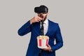 Bearded businessman in VR headset watching movie with popcorn, eating tasty snack.
