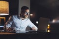 Bearded businessman wearing white shirt working on modern loft office at night. Man using contemporary notebook texting Royalty Free Stock Photo