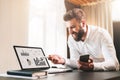 Bearded businessman in white shirt is sitting at table in front of computer, showing pen on laptop screen with graphis