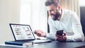 Bearded businessman in white shirt is sitting at table in front of computer, showing pen on laptop screen with graphis