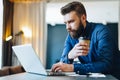 Bearded businessman working on computer at table,drinking coffee.Man analyzes information, data, develops business plan.