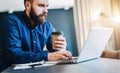 Bearded businessman working on computer at table,drinking coffee.Man analyzes information, data, develops business plan.