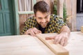 Bearded carpenter measuring wooden plank on table