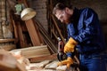 bearded carpenter in protective gloves and googles using electric drill