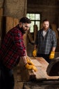 bearded carpenter in safety googles using machine saw and partner standing behind