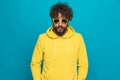 Bearded casual man wearing yellow hoodie and sunglasses confidently posing