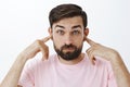 Bearded caucasian man close ears as standing in loud crowded place, holding index fingers in earholes pouting and Royalty Free Stock Photo