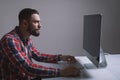 A bearded caucasian man is sitting behind the monitor of the computer. Muscular handsome guy is looking at the display during work Royalty Free Stock Photo