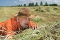 Bearded Caucasian senior farmer lying on stack of hay on agricultural field and looking forward