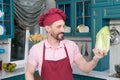Bearded Chef in red apron and hat holds and looks at napa cabbage on kitchen. pakchoi in hand of cook. Fresh Chinese leaves tested