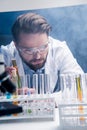 Bearded chemist in goggles with reagents in tubes in laboratory