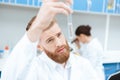 Bearded chemist in white coat examining test tube in laboratory