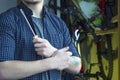 Bearded Classy Young Man with a Tattoo in a T-Shirt and Plaid Shirt Prepares To Maintenance Bicycle. Arms Crossed Holding Tools.