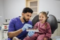 Bearded confident male dentist checking and selecting color of young caucasian girl's teeth. Royalty Free Stock Photo