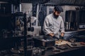 Bearded cook dressed in uniform and hat preparing sushi in kitchen.