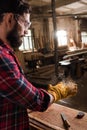 bearded craftsman in protective googles and gloves shaking off wooden chips from hands