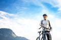 bearded cyclist stands with a bicycle against a background of blue sky and mountains. cycling and health-related hobbies Royalty Free Stock Photo