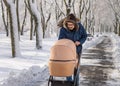 A bearded dad walking with baby carriage in winter park. A man with a baby stroller walks in a winter snow-covered city