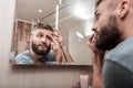 Bearded dark-haired man looking at acne on his face