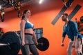 Bearded dark-haired trainer teaching plump woman to lift barbell