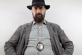 Bearded detective with hat and police badge looks down at the camera with her hands on her hips. Royalty Free Stock Photo