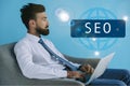 bearded developer using laptop and sitting in armchair on blue Royalty Free Stock Photo