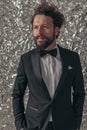 Bearded elegant groom in black tuxedo holding hands in pockets