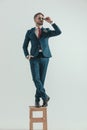 Bearded elegant man in suit standing on wooden chair and adjusting glasses