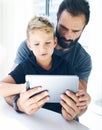 Bearded father with his young son using tablet PC in sunny room.Dad and little boy playing together on mobile computer, resting in Royalty Free Stock Photo